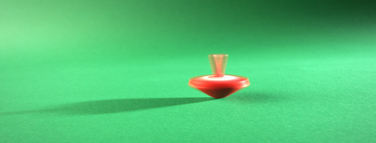 Ein sich drehender, roter Kreisel auf einem grünen Untergrund, mitten in der Bewegung eingefangen.