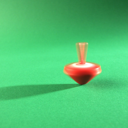 Ein sich drehender, roter Kreisel auf einem grünen Untergrund, mitten in der Bewegung eingefangen.