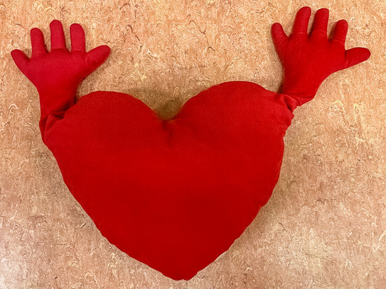 rotes Kissen in Herzform mit Händen 