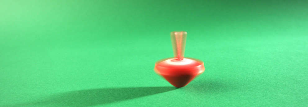 Ein sich drehender, roter Kreisel auf einem grünen Untergrund, mitten in der Bewegung eingefangen.