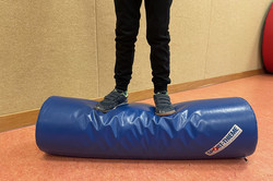 Ansicht der Beine eines Kindes in schwarzer Sporthose, steht auf einer blauen Gymnastikrolle